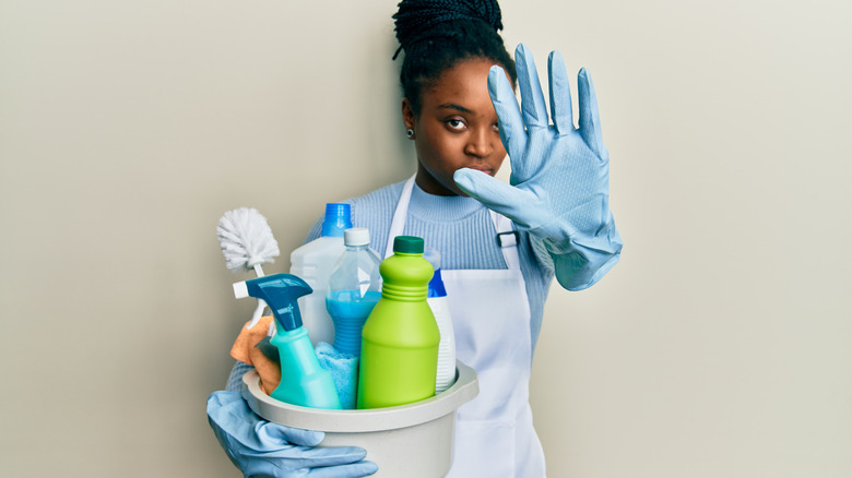 woman holding a bucket of cleaning products and gesturing "stop" with hands