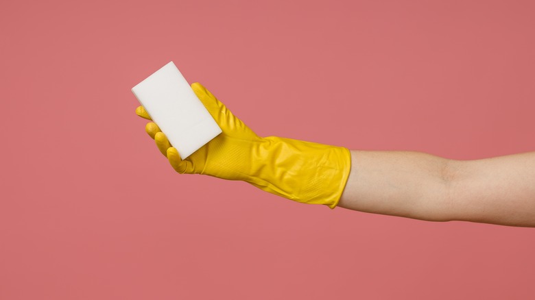 yellow gloved hand holds magic eraser pink background
