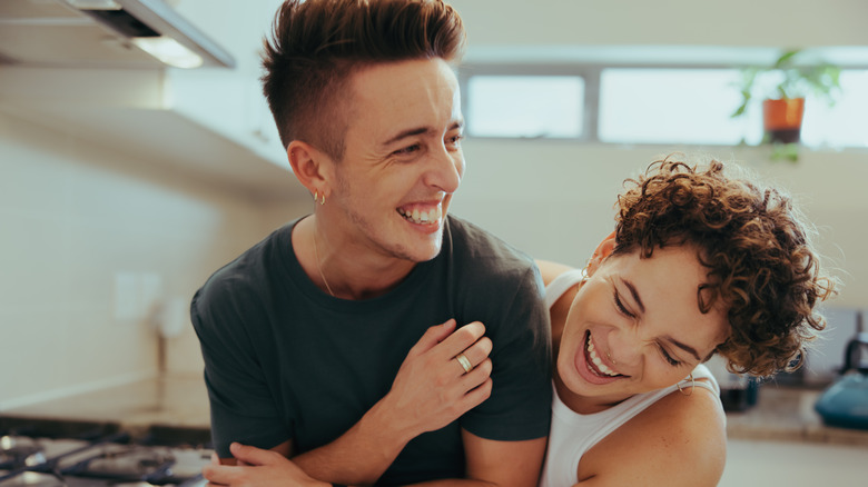 Queer couple in kitchen laughing 