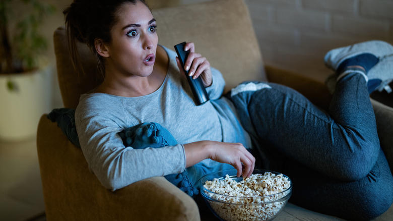 Woman eating popcorn and staring disbelievingly at television