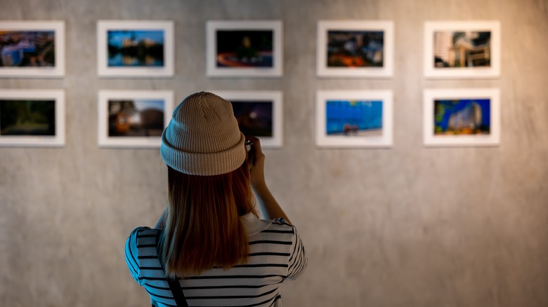 Woman photographing prints exhibited on wall