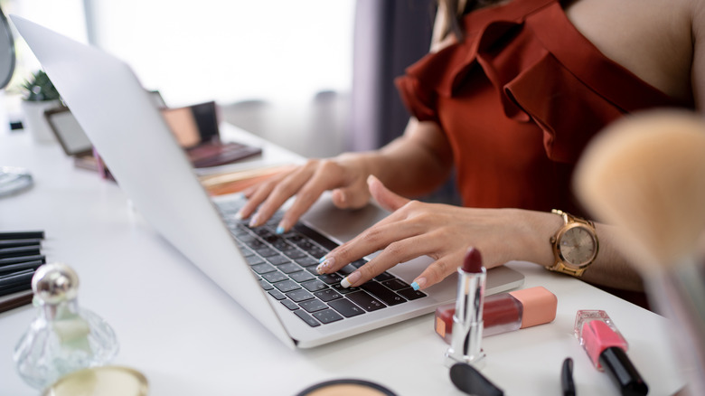 Woman typing on laptop near makeup