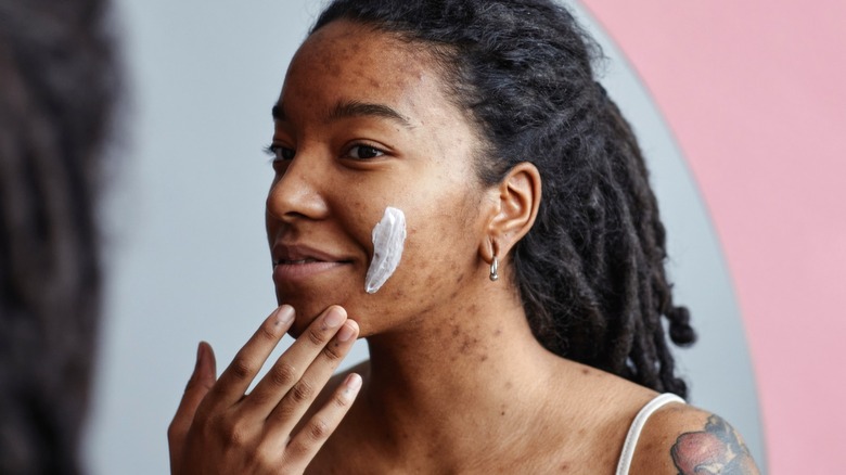 Woman with acne applying skincare