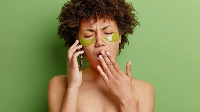 Bored woman performing undereye mask while on phone