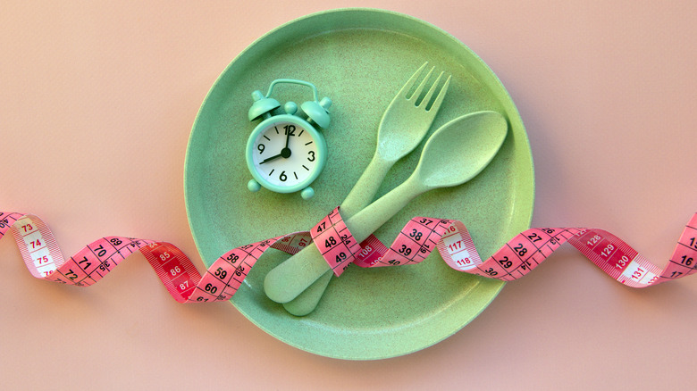 plate, cutlery, alarm, and tape, symbolizing intermittent fasting