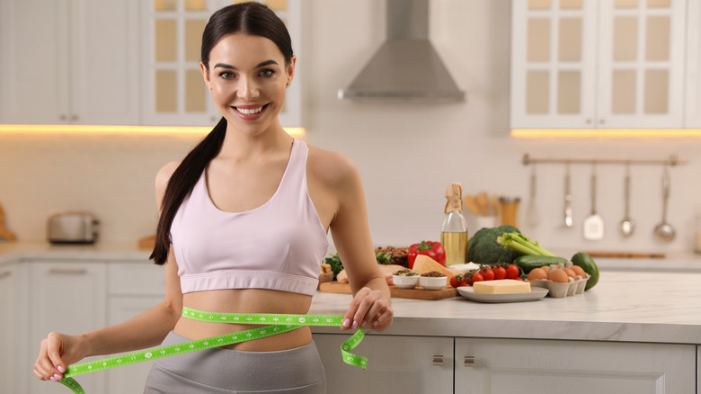 woman measuring waist in kitchen with keto foods on island