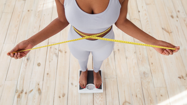 woman standing on scale and using measuring tape