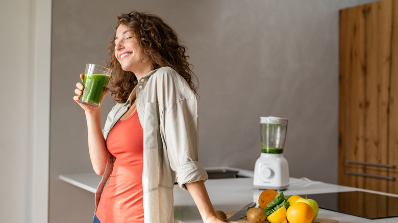 woman holding green juice in kitchen