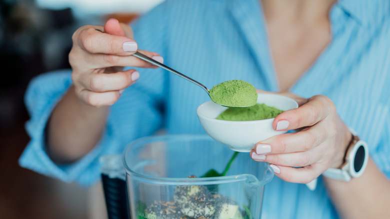 woman adding green powder to smoothie