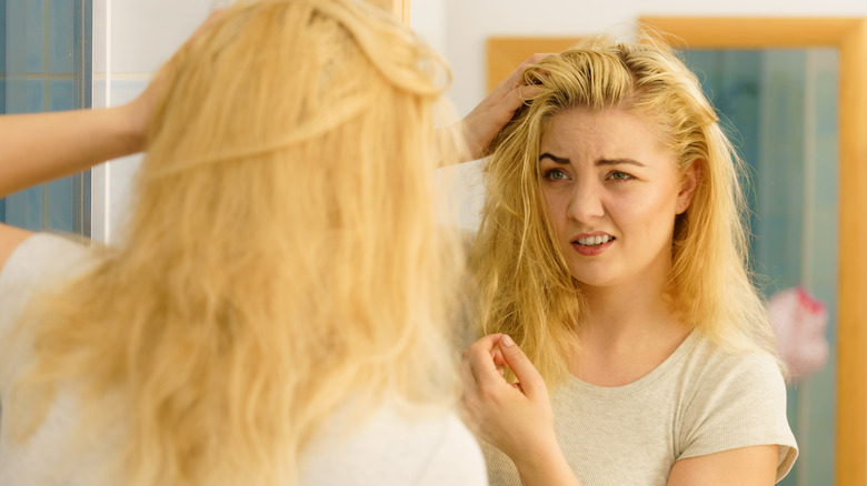 Woman examining oily hair in mirror