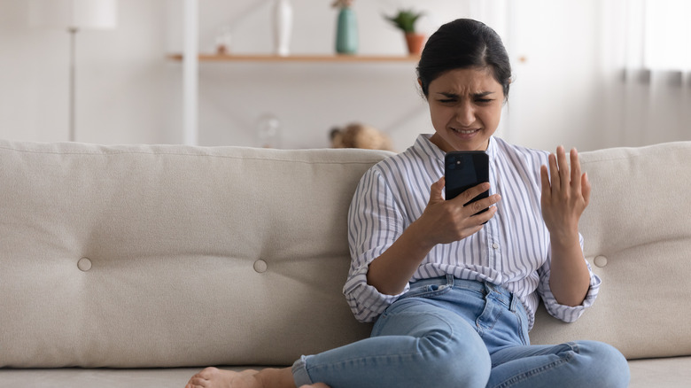 Indian woman sitting on her couch looking at her phone in disbelief