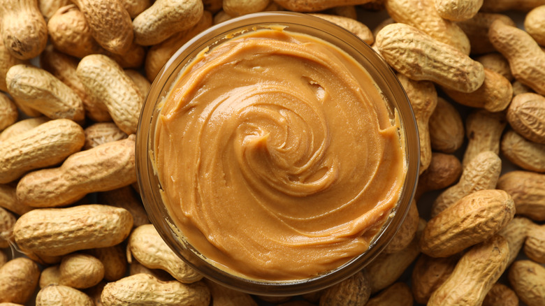 Jar of peanut butter surrounded by peanuts