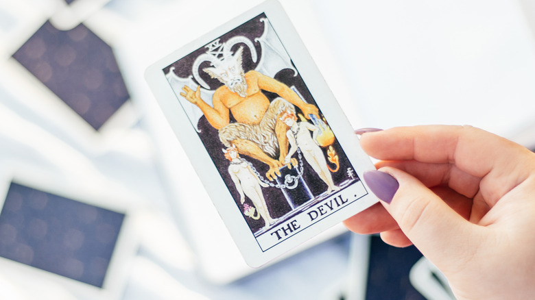 Woman's hand holding devil tarot card