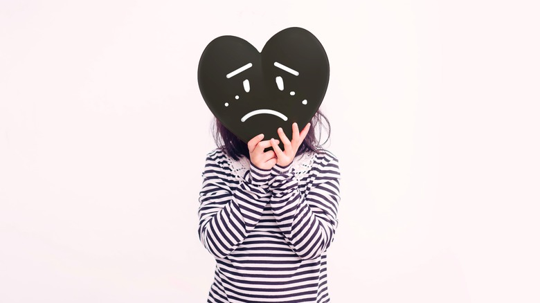 Person holding a a heart with a sad expression in front of their face