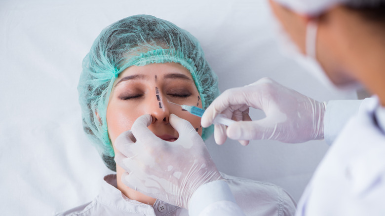 Surgeon with needle near woman's nose