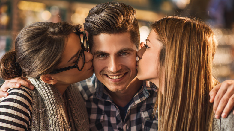 Two women kissing man's cheeks