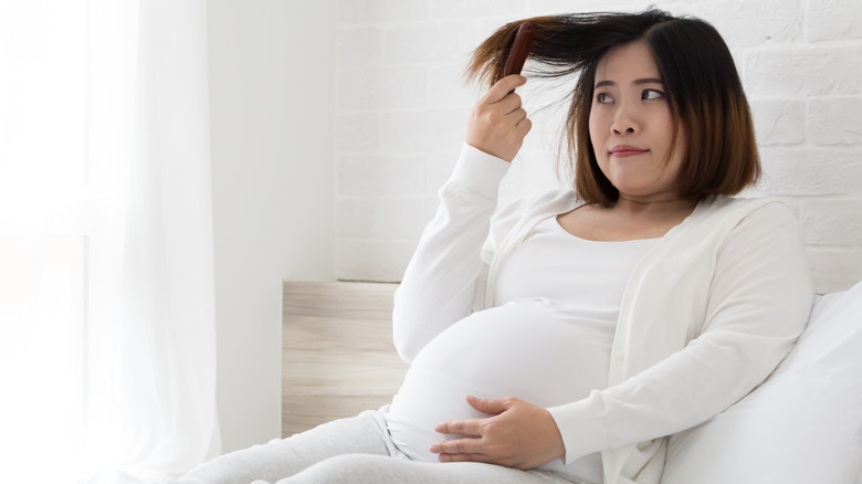 Pregnant woman brushing hair on bed