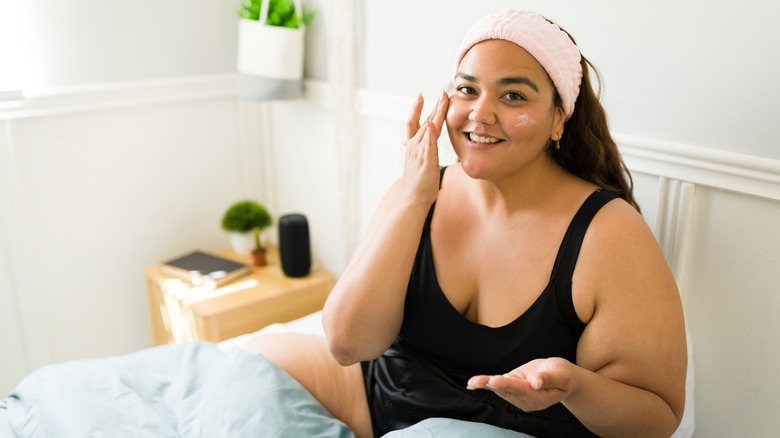 Woman applying skincare in bed