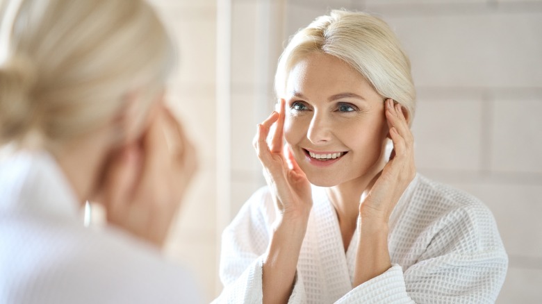 smiling middle aged woman touching face in mirror