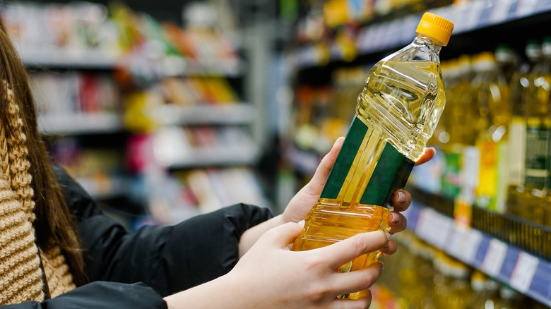 Woman picking up sunflower oil from grocery store shelf