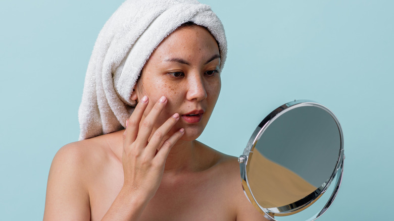 Woman examining signs of sun damage in front of mirror