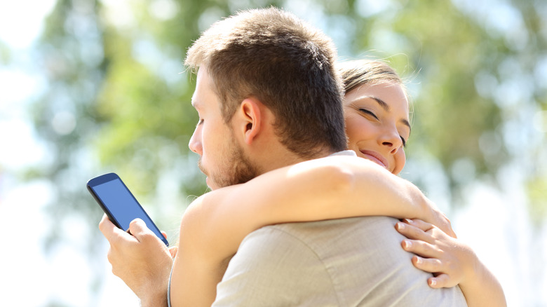 Man texting while hugging woman