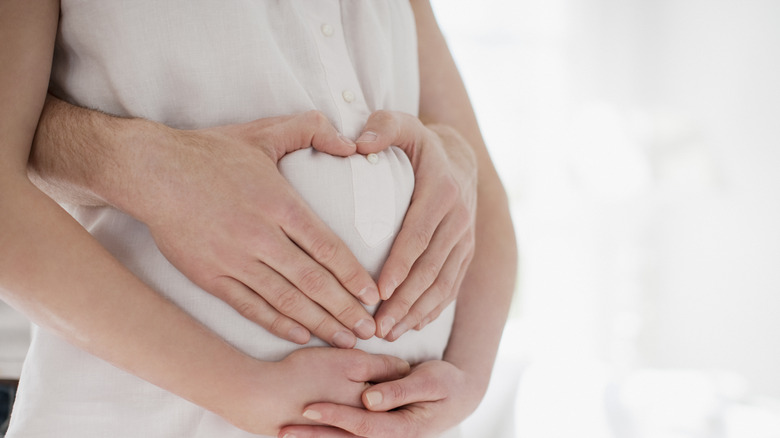 Man makes a heart with his hands over pregnant woman's belly