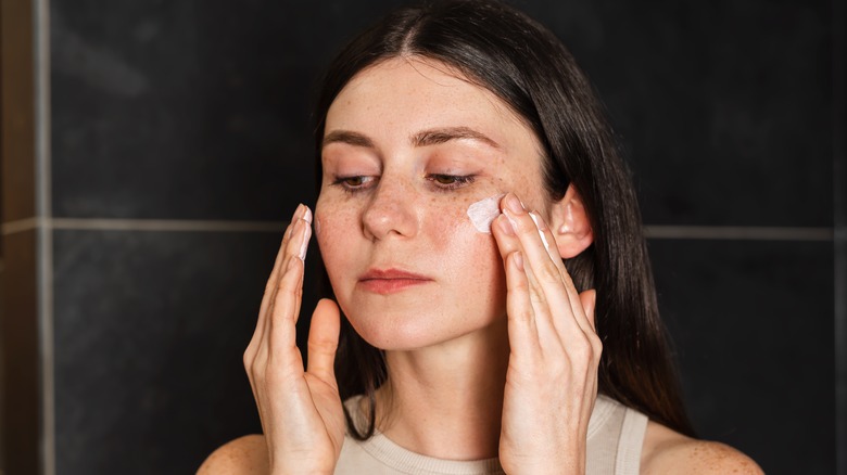 Woman applying moisturizer to face