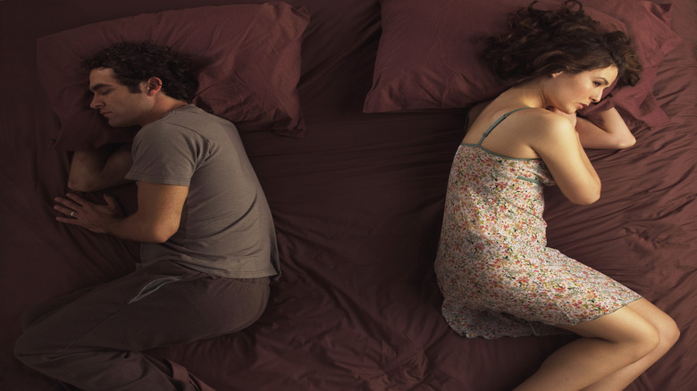 An unhappy couple laying in bed with their backs turned.