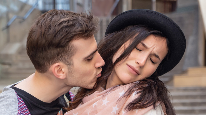 A woman leaning away from a man trying to kiss her.