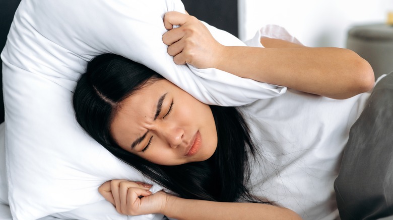 Emotional woman hides under pillow