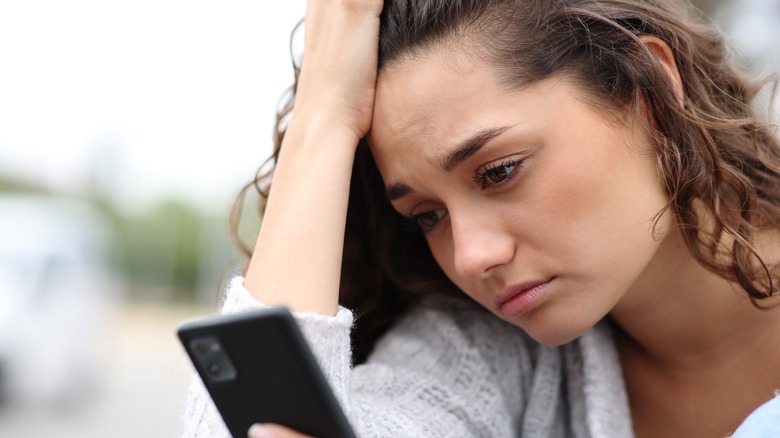 Woman checking her phone looking sad