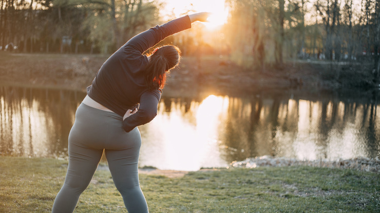 Woman stretching by sunrise pond