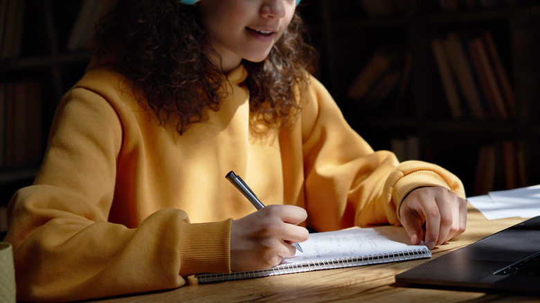 Woman in yellow sweatshirt writing in a notebook