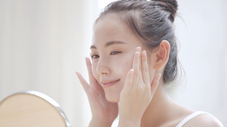 woman looking at skin in mirror