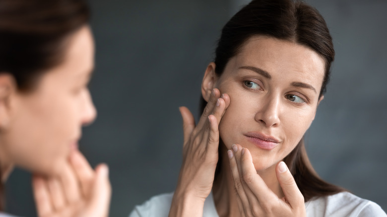 woman looking at skin in mirror