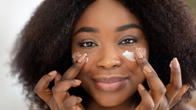 woman applying moisturizer to cheeks