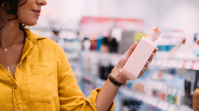 A person looking at a beauty product and trying to decide whether to buy it in a store.