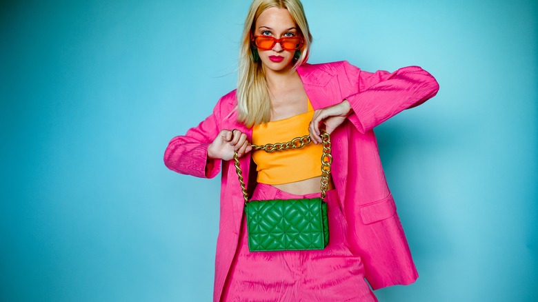 Woman in pink blazer and yellow tank top, holding green purse