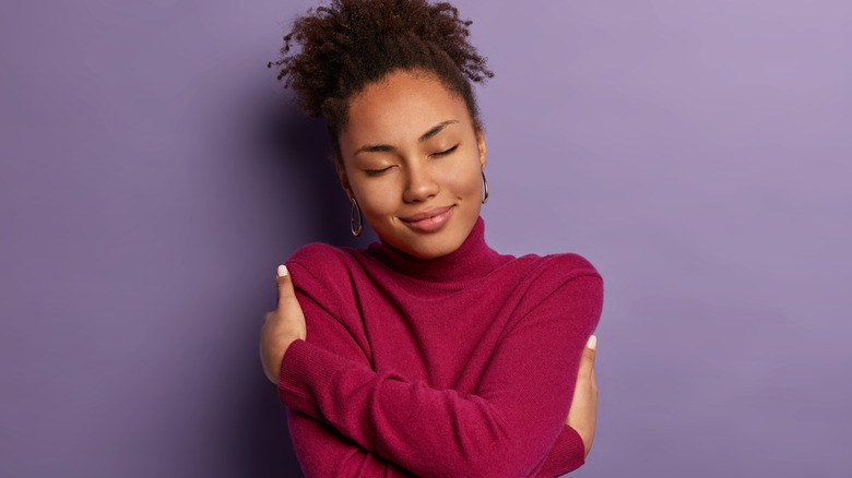 african american woman with curly hair in bun hugging herself