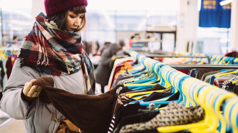 Woman glancing at sweater while perusing secondhand clothing