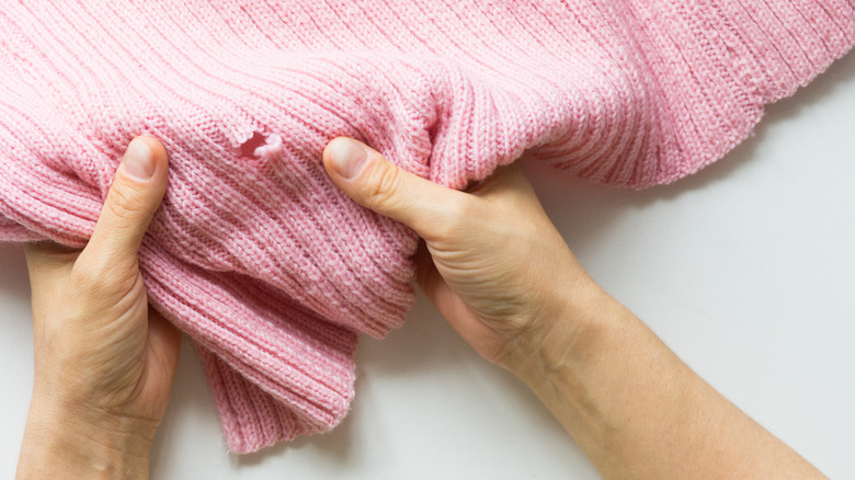 Person examining pink sweater with defect or moth hole