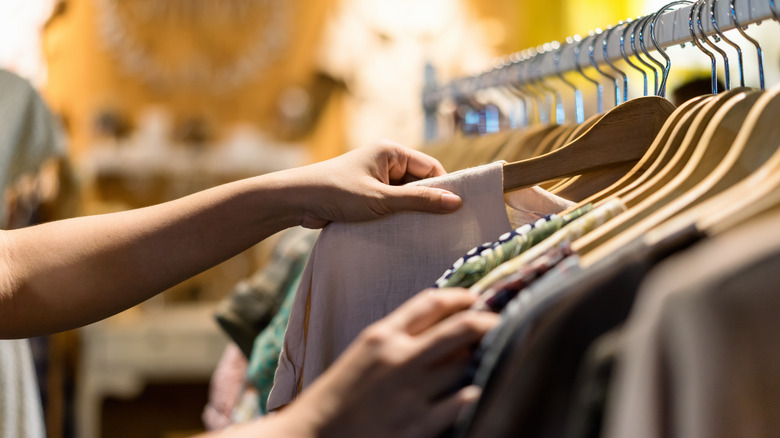 Person scanning through garment rack at thrift store