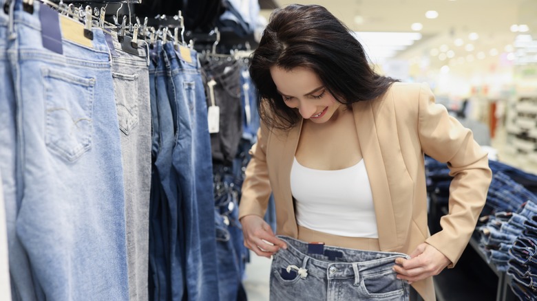 Girl measuring jeans against waist in clothing store