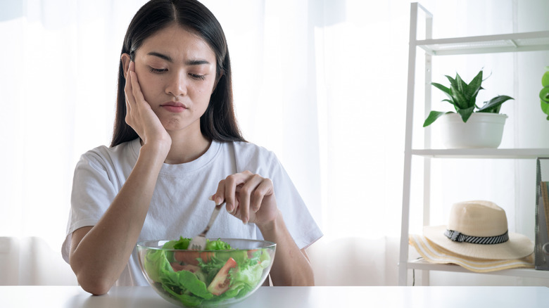 Woman hesitantly eating salad 