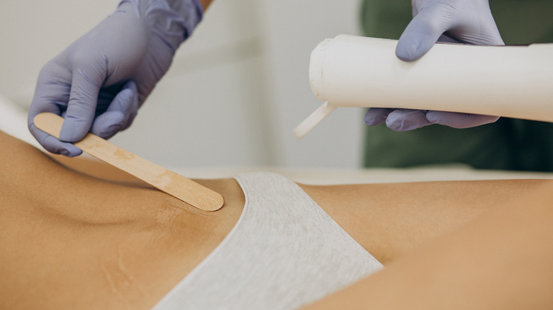 estheticians hands applying wax on lady's midrif