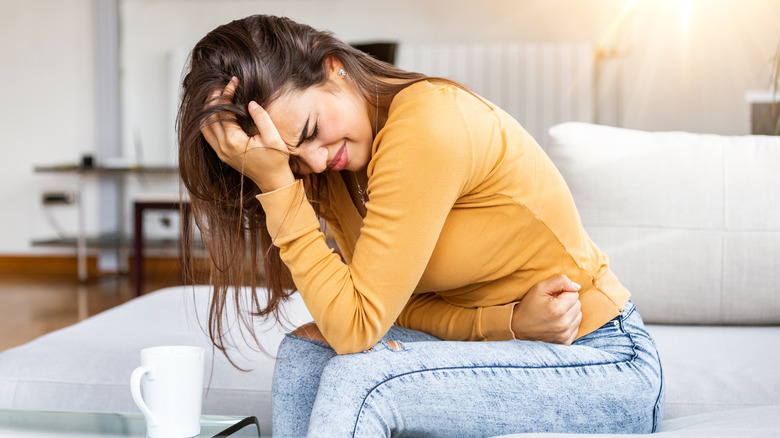 Woman sitting on couch holding stomach