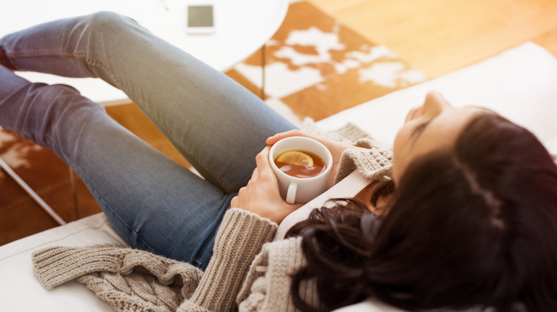 Woman in skinny jeans sitting on couch with coffee