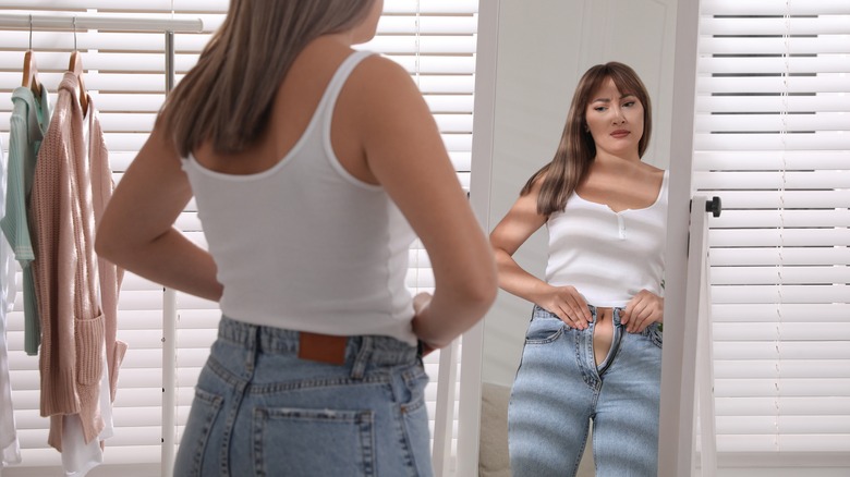 Woman looking in mirror trying to zip tight jeans