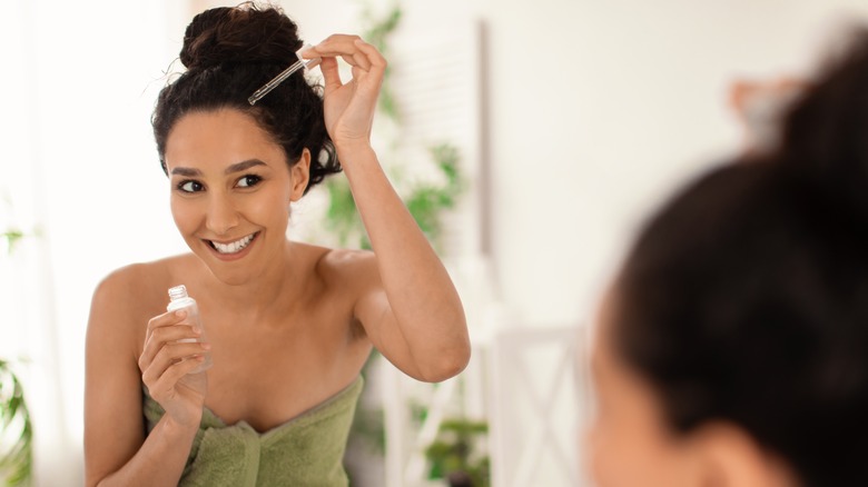 person applying serum to scalp in mirror